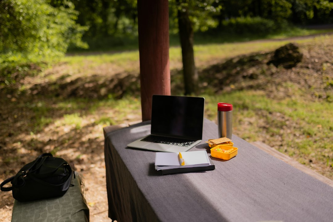 A laptop and notebook set up outdoors on a picnic table